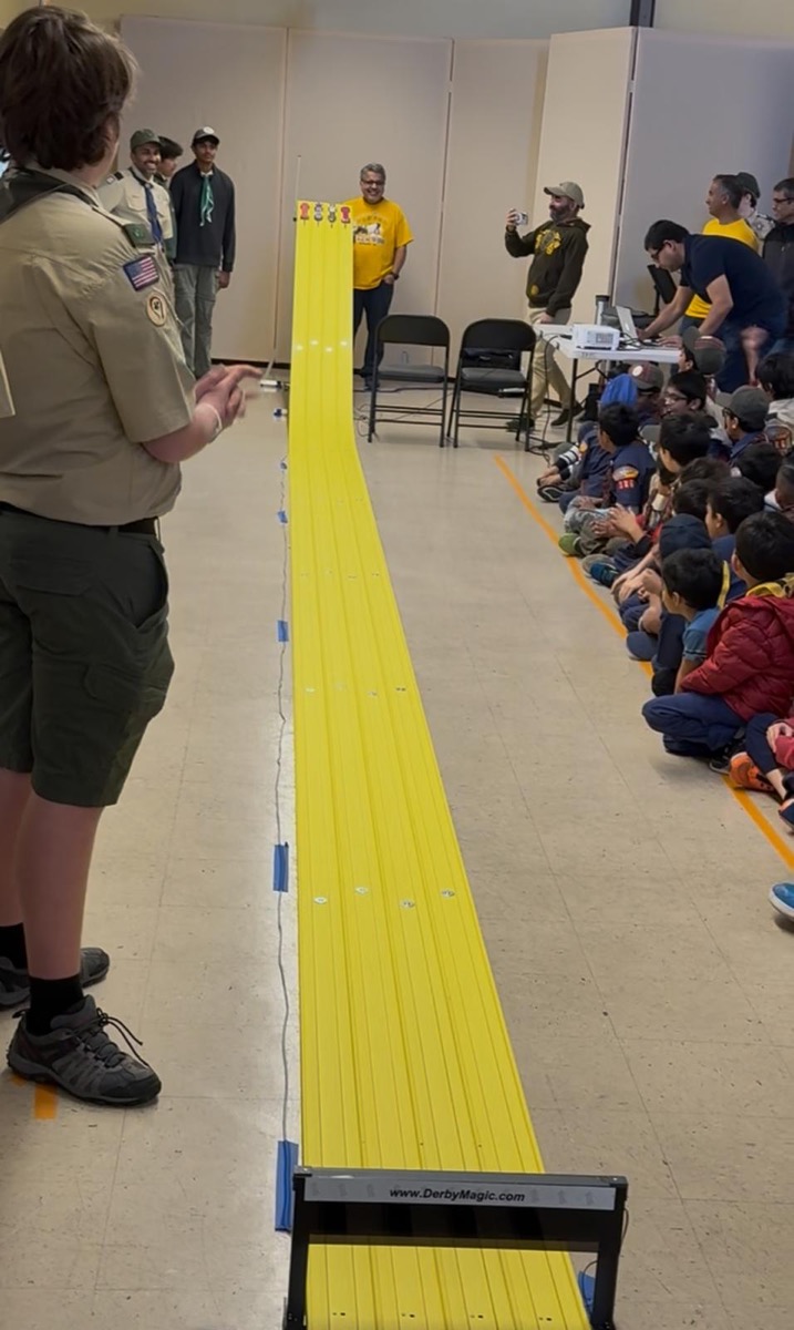 Scouts watching Pinewood Derby cars race down the track