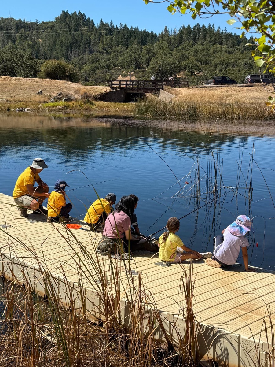 Scouts fishing off a dock at a sunny campsite lake